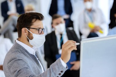 Male entrepreneur with protective face mask holding a seminar to group of people in convention center.