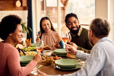 Multi-ethnic group of people drinking wine and communicating while having lunch in dining room. Focus is on black man. 