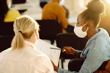 Black university student and her friend wearing protective face masks while going through test results in the classroom. 