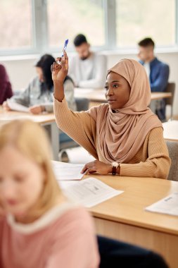 Female Islamic student raising her arm to ask a question on a class at the university. 
