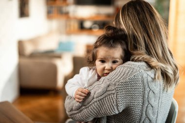 Loving mother embracing her small daughter at home. Focus in on daughter. 