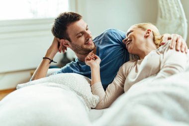 Happy couple lying down in bed and having fun while communicating in the morning. 