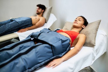 Young woman and her boyfriend enjoying in pressotherapy at wellness center. Focus is on woman.