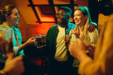 Group of happy friends having fun and toasting while gathering in a bar at night. 
