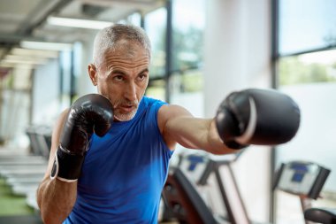 Mature man exercises boxing during sports training at gym.