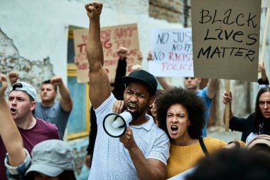 Multi-ethnic crowd of people fighting for freedom on a protest against racial discrimination. Focus is on African American couple shouting through megaphone. 