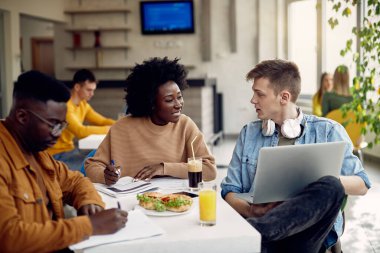 Multi-ethnic group of happy college students learning during lunch break in cafeteria.
