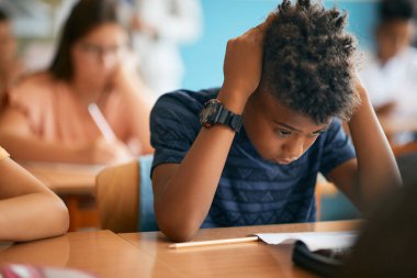 Black elementary student thinking while reading exam paper during a class at school.