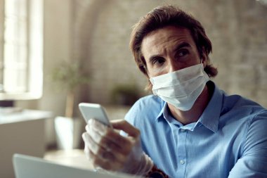 Distraught businessman using mobile phone and thinking while working in the office during coronavirus epidemic.