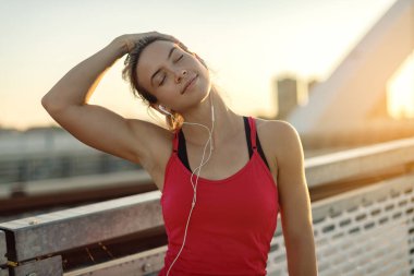 Young athletic woman warming up and stretching her neck at sunset. 