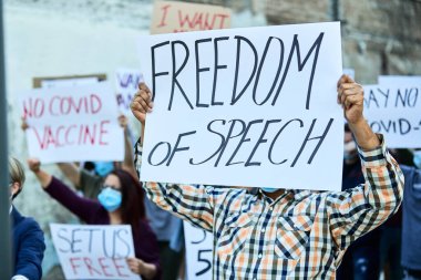 Unrecognizable man with freedom of speech banner marching with group of people on a protest during coronavirus pandemic. 