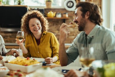 Young cheerful woman and her boyfriend communicating while eating and drinking wine at dining table. 