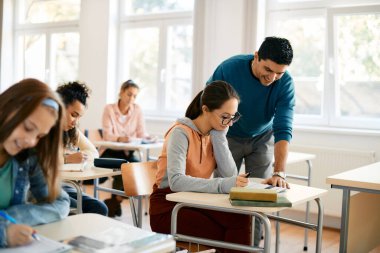 Happy professor assisting his student with a lecture during class at high school.