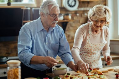 Senior man and his wife enjoying in preparing food in their kitchen. 