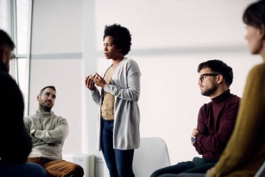Black woman attending group therapy and sharing her problems with the participants. 
