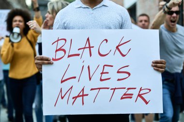 Unrecognizable man holding Black Lives Matter placard while participating on a protest on city streets. 