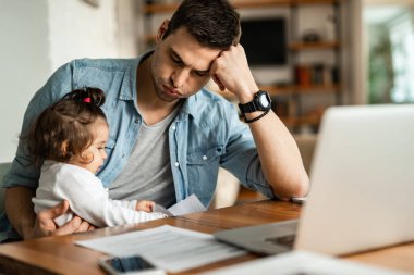 Stay at home father feeling tired while trying to work and babysitting his small daughter. 