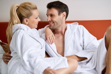 Smiling couple in love talking while relaxing on a bed in hotel room. 