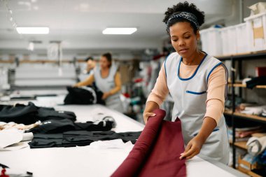 African American textile worker using new fabric roll while working at tailor's.