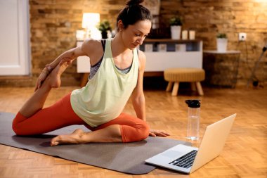 Athletic woman doing stretching exercises while watching video tutorial over laptop at home. 