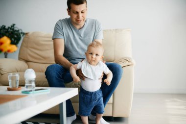 Cute baby boy standing with assistance of his father at home.