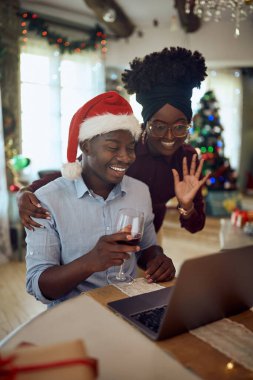 Happy black couple using laptop and talking to someone via video call on Christmas at home. 