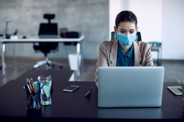 Female entrepreneur wearing protective face mask while working on laptop in the office.