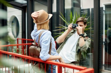 Tourist couple having fun while being on a vacation. Man is using photo camera and taking picture of his girlfriend.