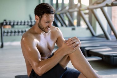 Male athlete holding his knee in pain during sports training in a gym. 