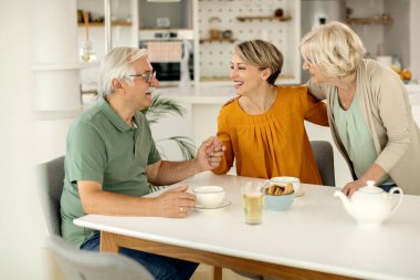 Happy mature couple communicating with their adult daughter who is visiting them at home. 