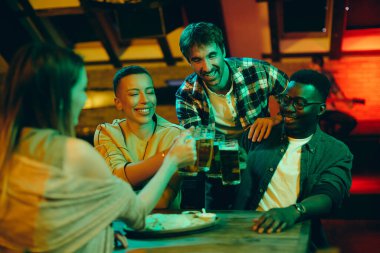 Group of young happy people having fun while toasting with beer in a bar at night. 