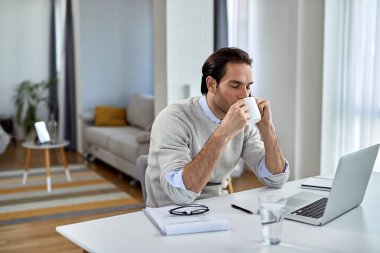 Young entrepreneur talking on mobile phone while having coffee break at home. 