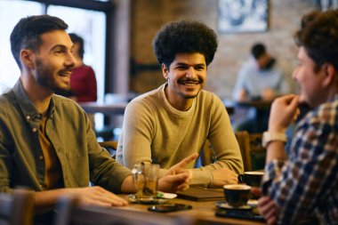 Multiracial group of young men talking while gathering in a cafe. Focus is on Muslim man. 