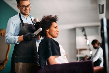 Smiling black woman enjoying while getting hair treatment at hairdresser's. 