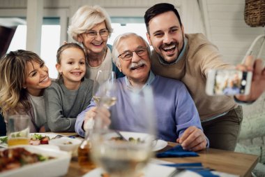 Happy extended family having fun while taking selfie with smart phone at dining table. 
