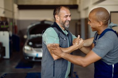 Happy coworkers greeting each other with manly greet while working in car service workshop. 