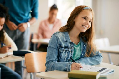 Smiling high school student writing in notebook while learning in the classroom.