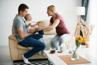 Happy mother dressing up her baby boy while father is holding him at home.
