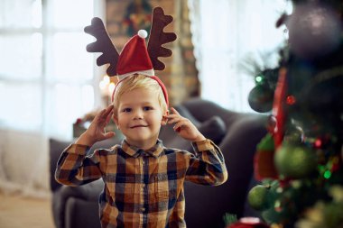 Smiling little boy with reindeer antlers for Christmas at home and looking at camera.