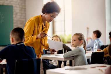 Black elementary school teacher explaining test results to a student in the classroom. 