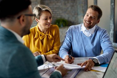 Happy couple signing paperwork while having a meeting with financial advisor in the office. 