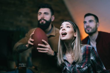 Young woman and her friends watching rugby match on TV with anticipation.
