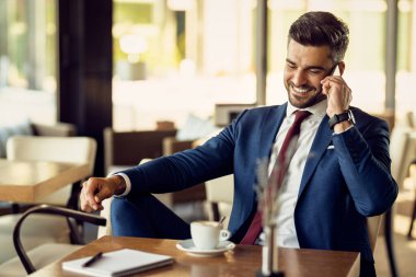 Happy male entrepreneur using phone and talking to someone during coffee break in a cafe. 