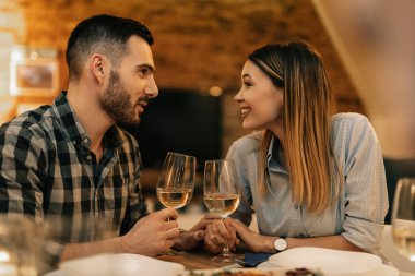 Happy couple communicating while having dinner and drinking wine in dining room.
