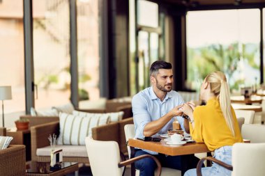 Smiling man and his girlfriend holding hands and communicating in a cafe. 