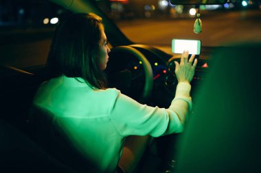 Gece araba kullanırken akıllı telefonda navigasyon yazılımı kullanan bir kadının arka görünümü. 