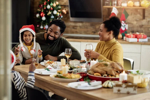 Happy black parents and their kids communicating having family lunch on Christmas day in dining room.