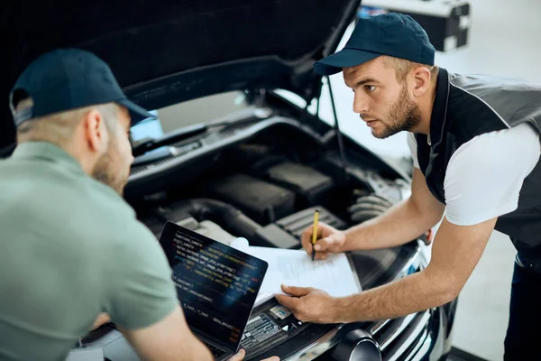 Auto Repairman Writing Data Talking His Coworker Who Using Laptop — Φωτογραφία Αρχείου