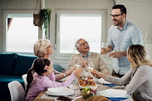 Cheerful mid adult man holding a toast while having lunch with his family in dining room.