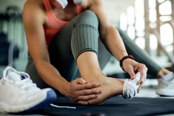 Close-up of female athlete holding her ankle in pain after exercising in health club.